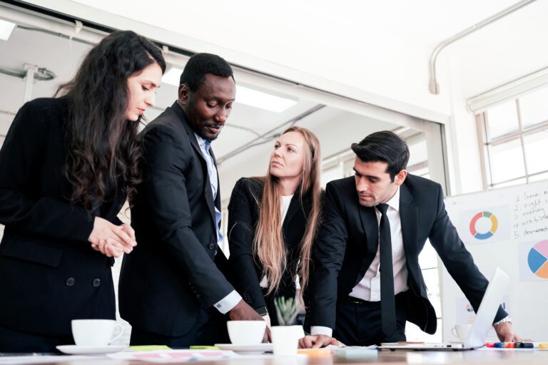 Four colleagues leaning over a desk discussing a project.