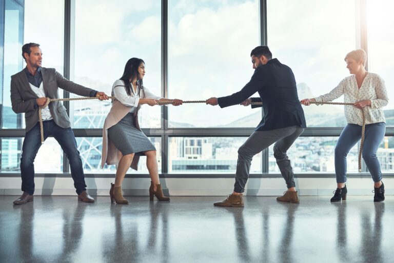 Two teams of business colleagues pulling a rope in a tug-of-war game in an office.