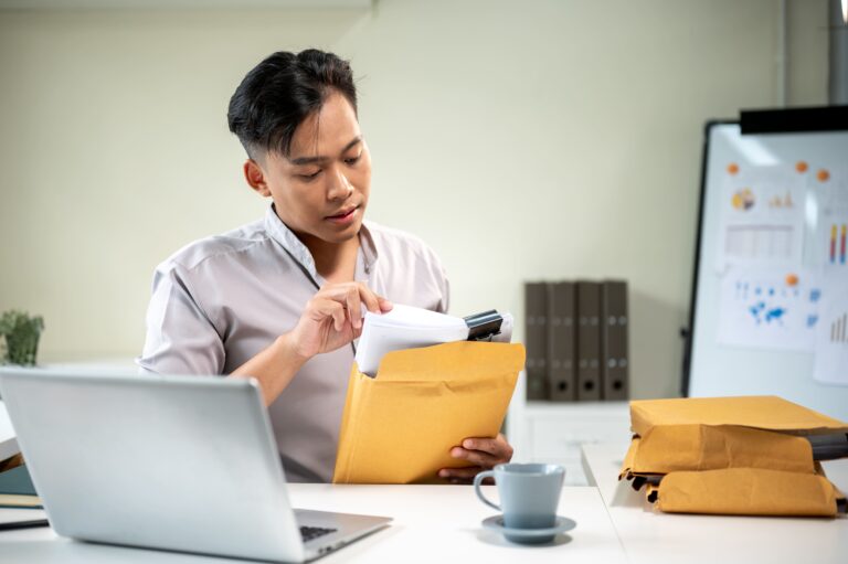 A man seated at a desk opening a large manila envelope.