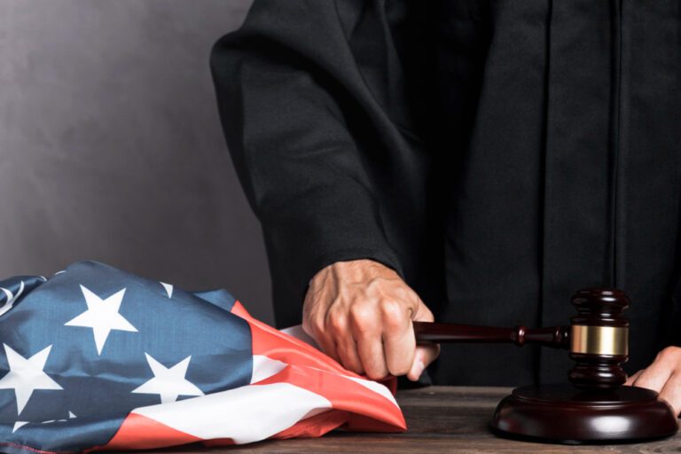 A judge's hand holding a gavel next to an American flag.